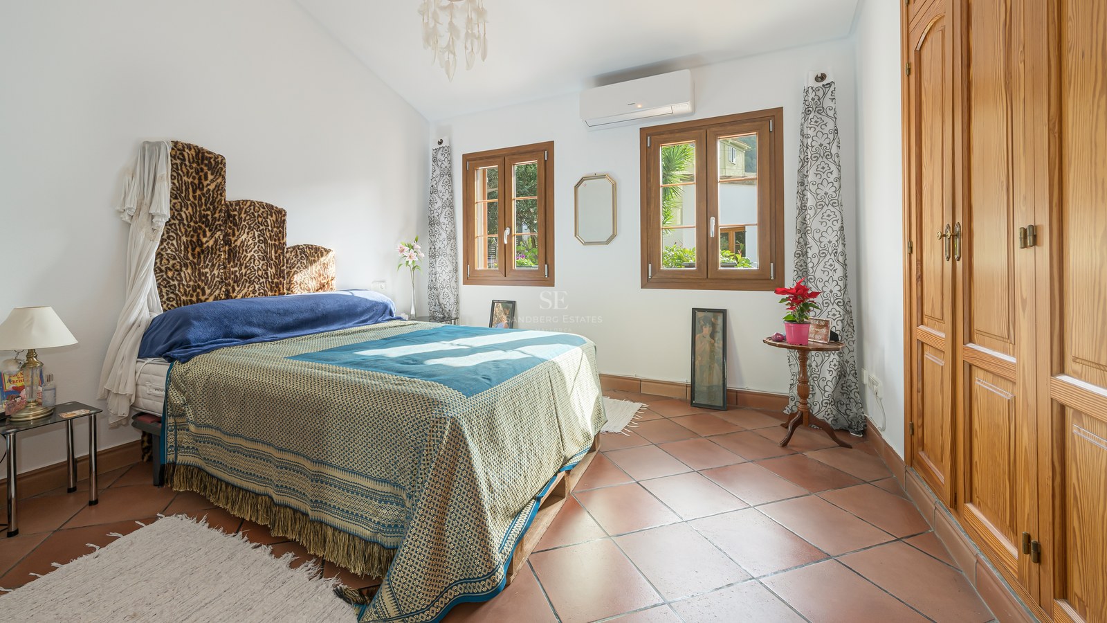 Chambre ensoleillée avec sol en terre cuite, grandes armoires en bois et fenêtres donnant sur la verdure.