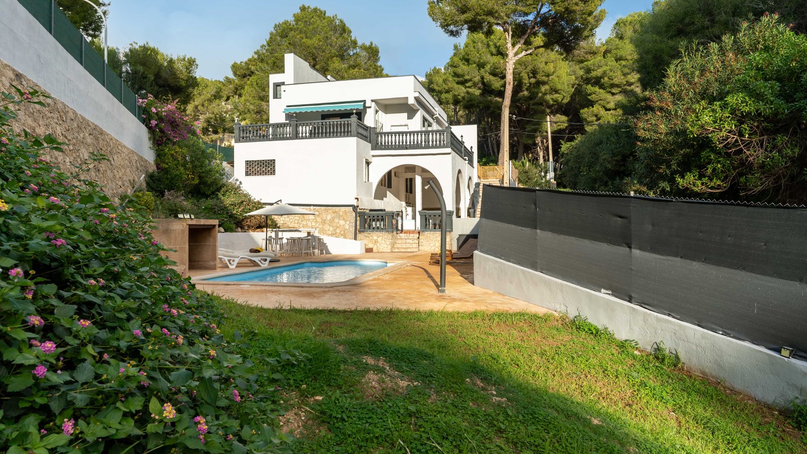 White multi-story villa featuring a private swimming pool, sun terrace, and lawn surrounded by a lush pine forest.