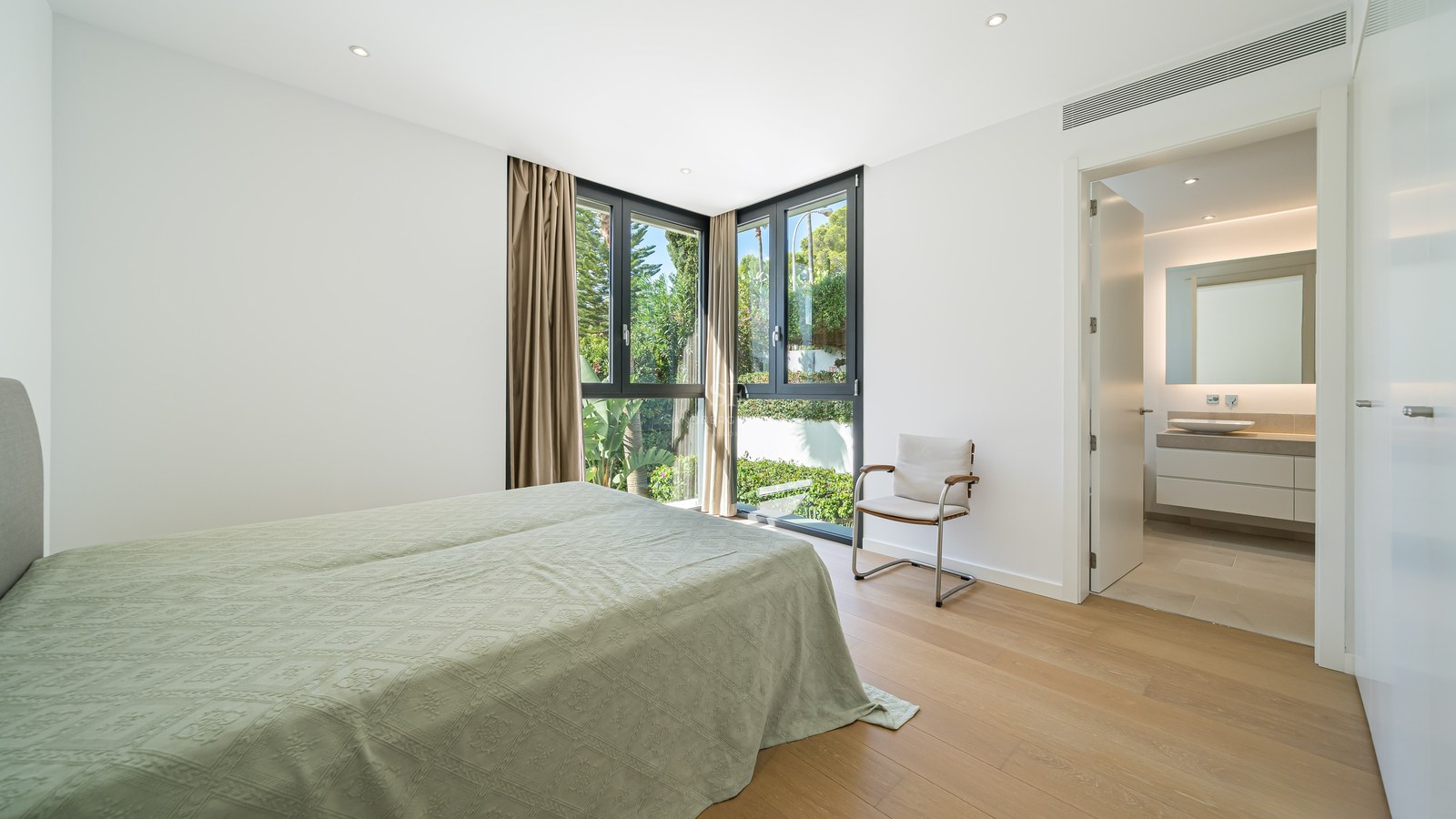 Chambre de maître lumineuse avec parquet, fenêtres d'angle et salle de bain moderne attenante.