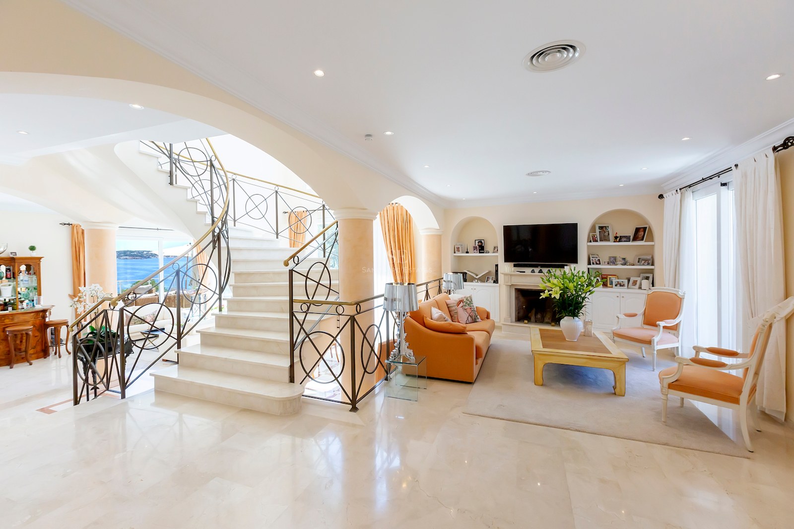 Spacious living room featuring a grand marble staircase, arched windows with sea views, and a classic fireplace.
