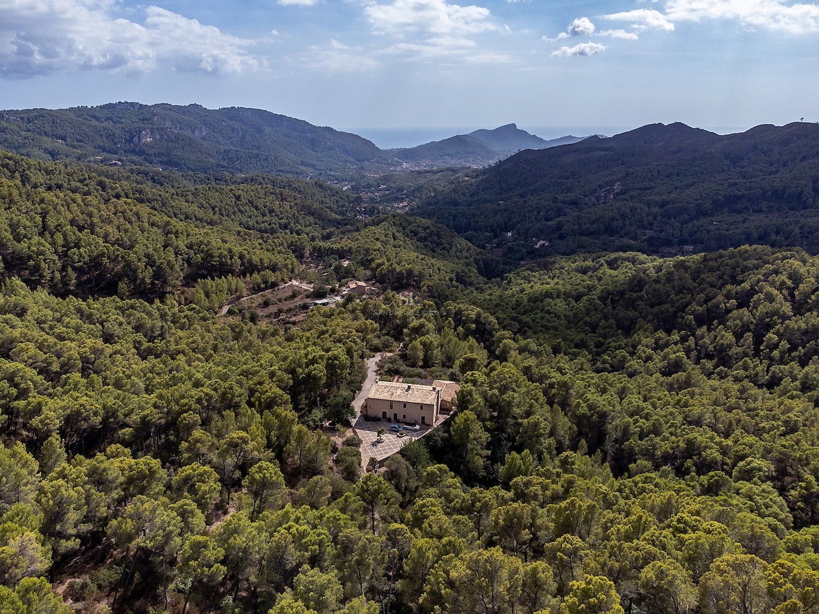 Vue aérienne d'une villa privée entourée d'une forêt verdoyante dans une vallée avec vue sur la mer au loin.