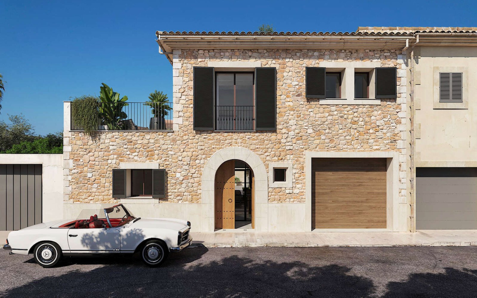 Maison de village en pierre avec porte voûtée, volets sombres et cabriolet Mercedes classique blanc stationné devant.