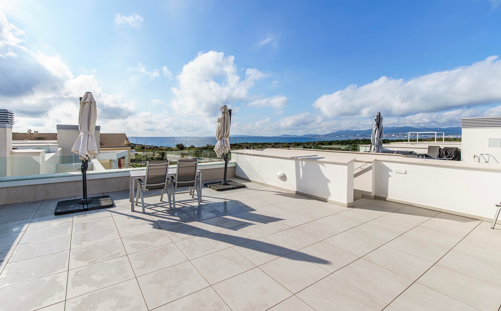 Grande terrasse moderne avec carrelage blanc, garde-corps en verre et coin repas avec vue sur la mer bleue.