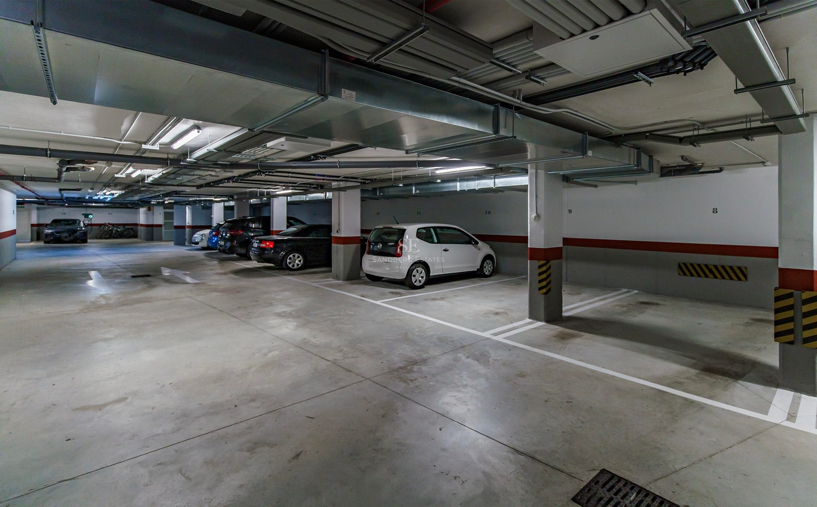 Parking souterrain éclairé avec places numérotées et voitures garées sous des conduits de ventilation.