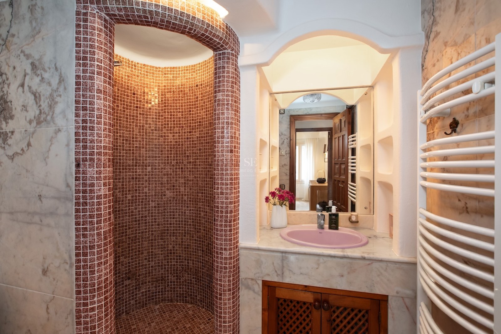 Douche à l'italienne courbe en mosaïque rougeâtre à côté d'un meuble vasque en marbre avec un évier rose.