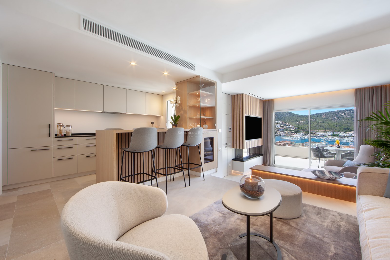 A bright, modern open-plan living room and kitchen featuring beige cabinetry, an island with stools, and a large window with a marina view.