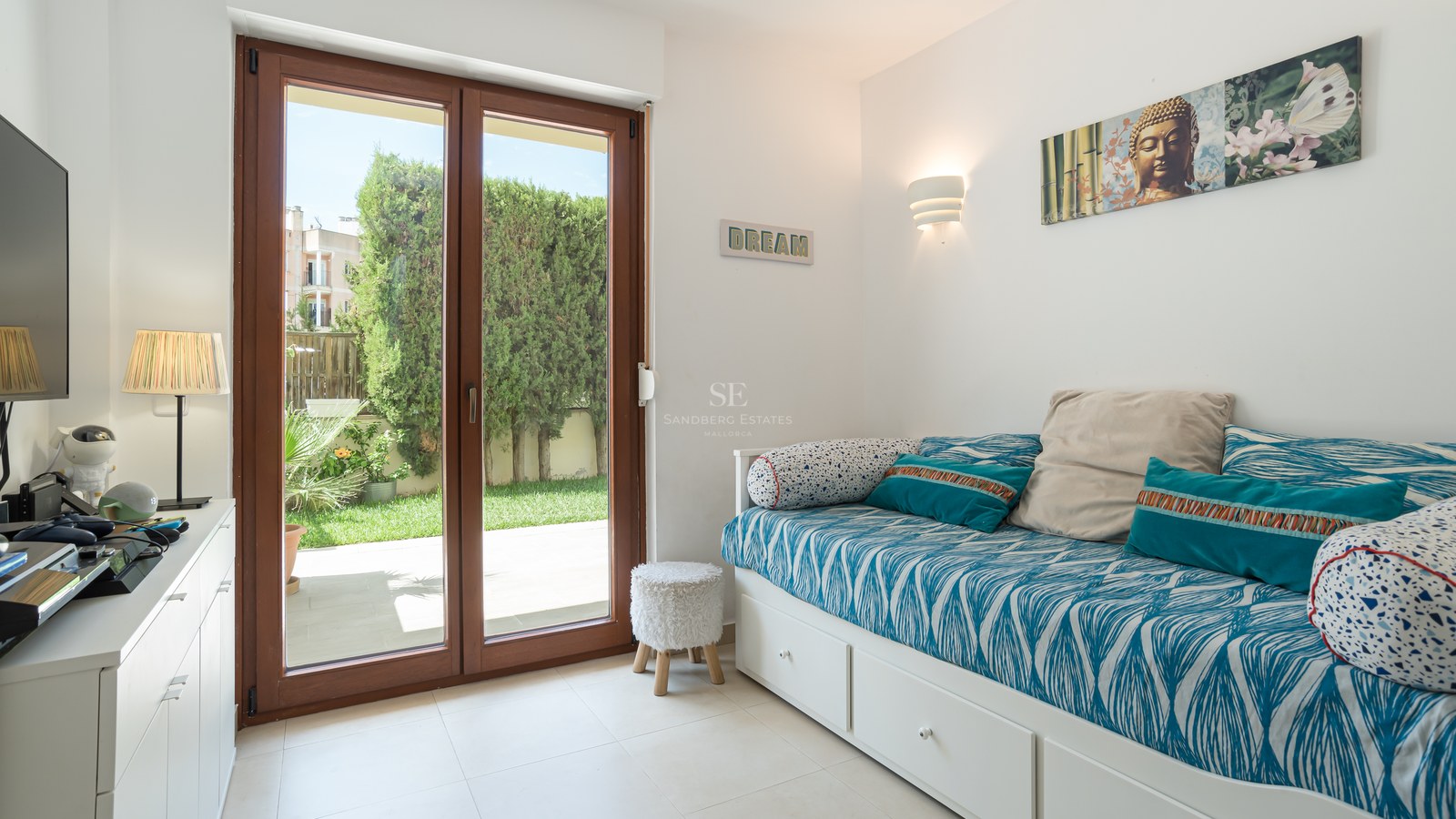 Dormitorio moderno con cama nido blanca y puertas correderas de madera hacia un jardín privado con setos verdes.