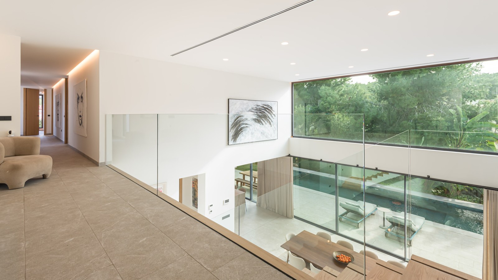 Vue depuis une mezzanine en verre sur un salon à double hauteur avec de grandes baies vitrées donnant sur la piscine.