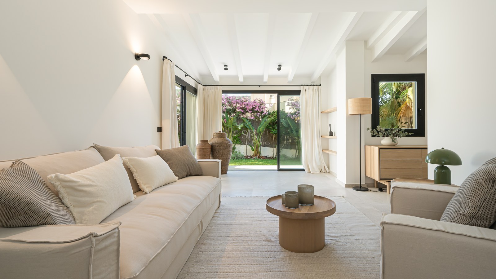 Salon lumineux avec canapés beiges et grandes baies vitrées ouvrant sur un jardin privé.