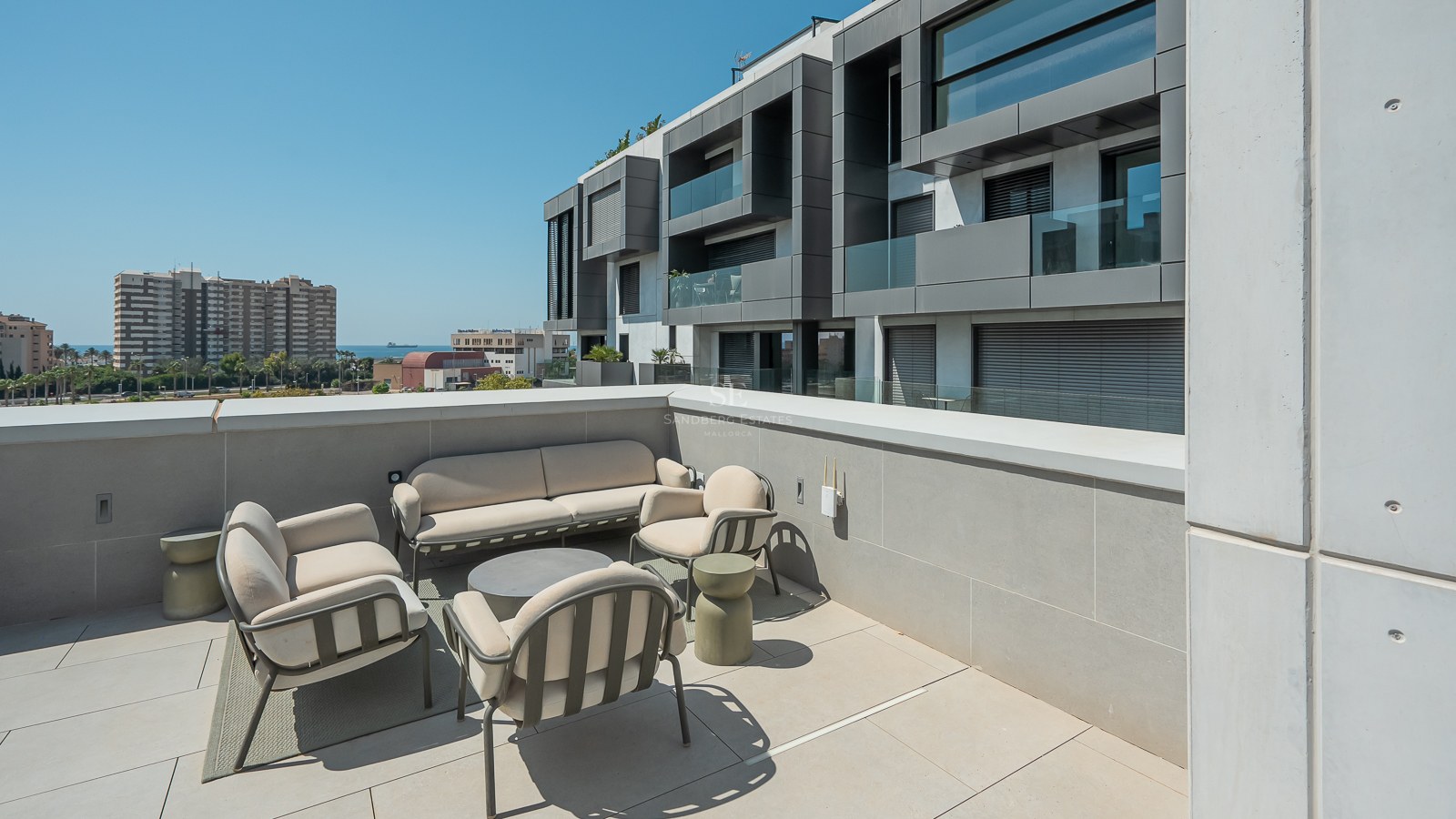 Une grande terrasse moderne avec du mobilier d'extérieur beige, un sol en carrelage gris et vue sur un bâtiment contemporain.