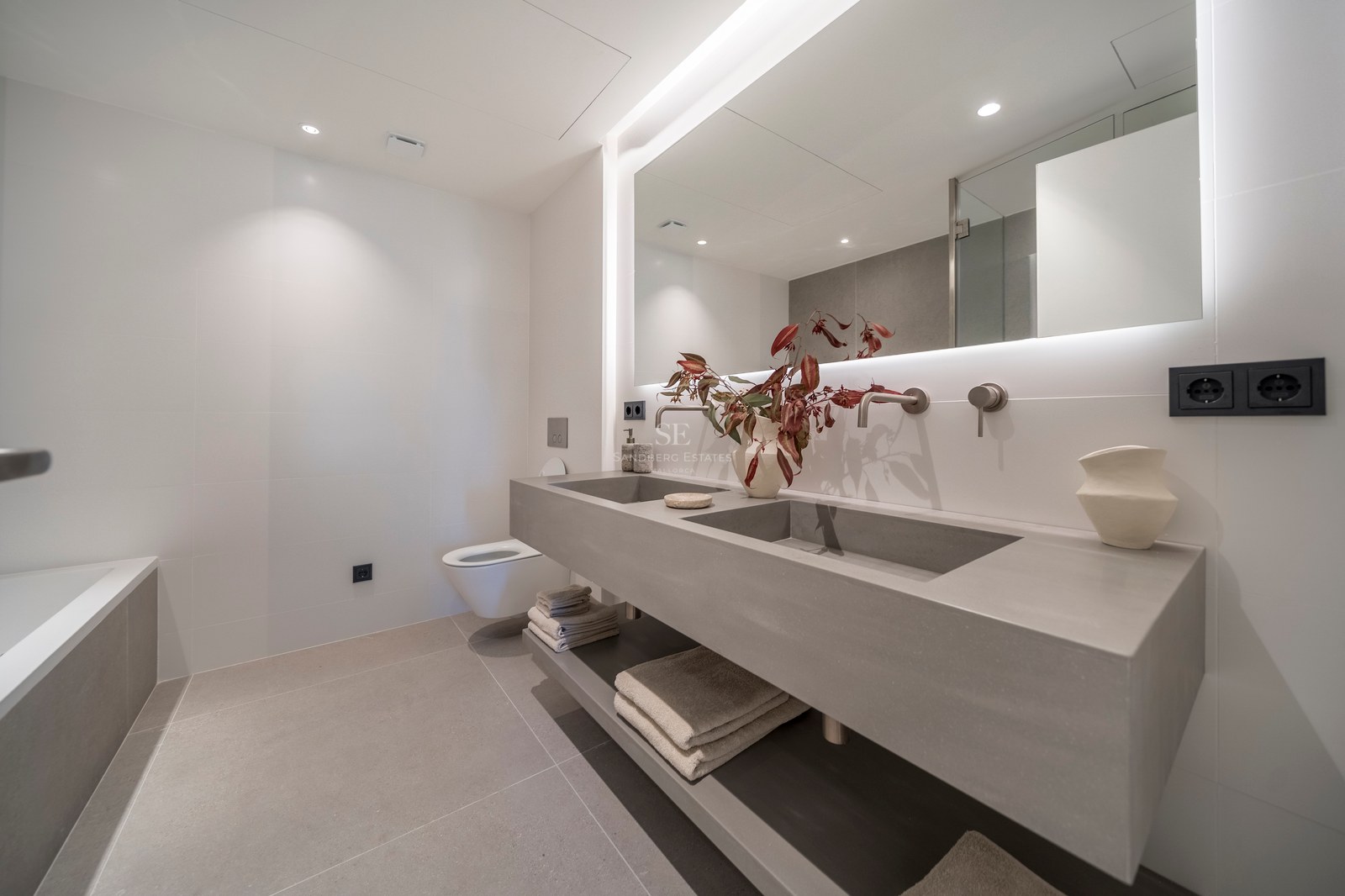 Salle de bain minimaliste avec double vasque flottante grise, grand miroir rétroéclairé et robinetterie murale.