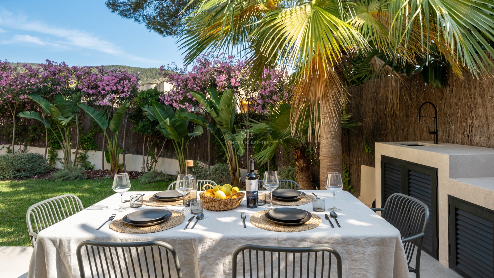 Table à manger extérieure pour six dans un jardin tropical à côté d'une cuisine d'été moderne en pierre.