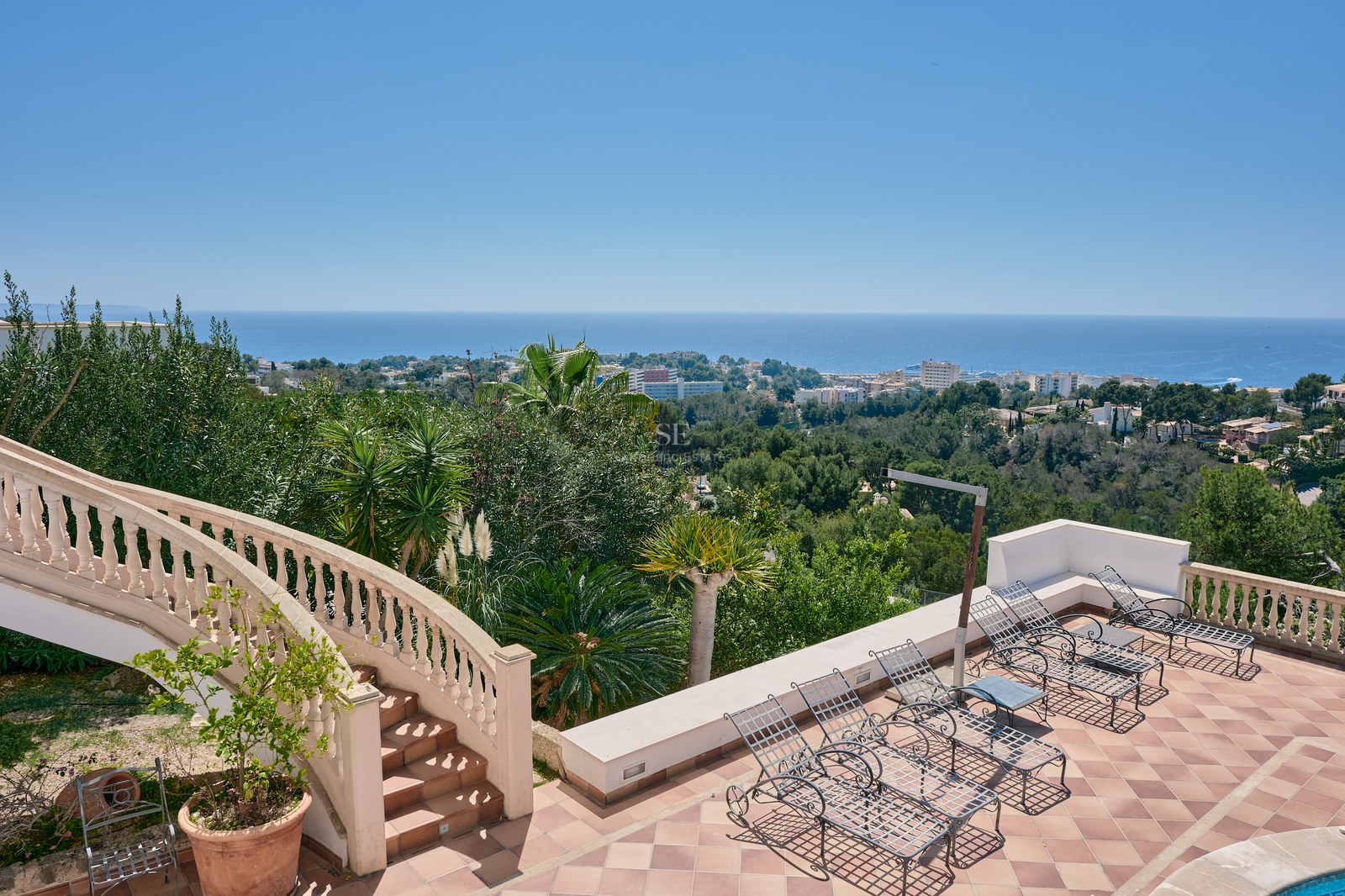 Terracotta terrace with wrought iron loungers and a classic stone staircase overlooking the Mediterranean sea.