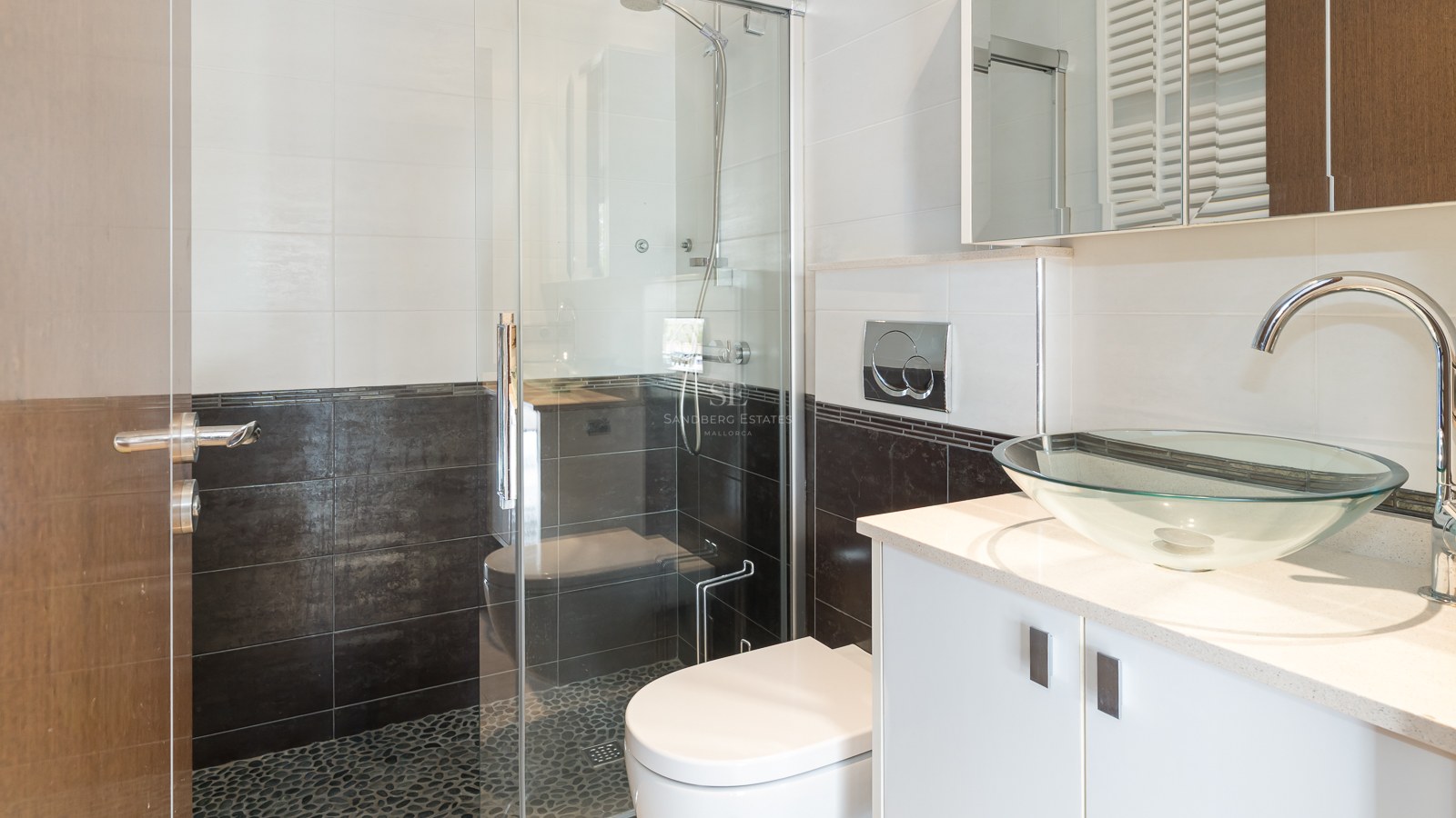Modern bathroom featuring a glass bowl sink, white vanity, and a glass-enclosed shower with pebble tile floor.