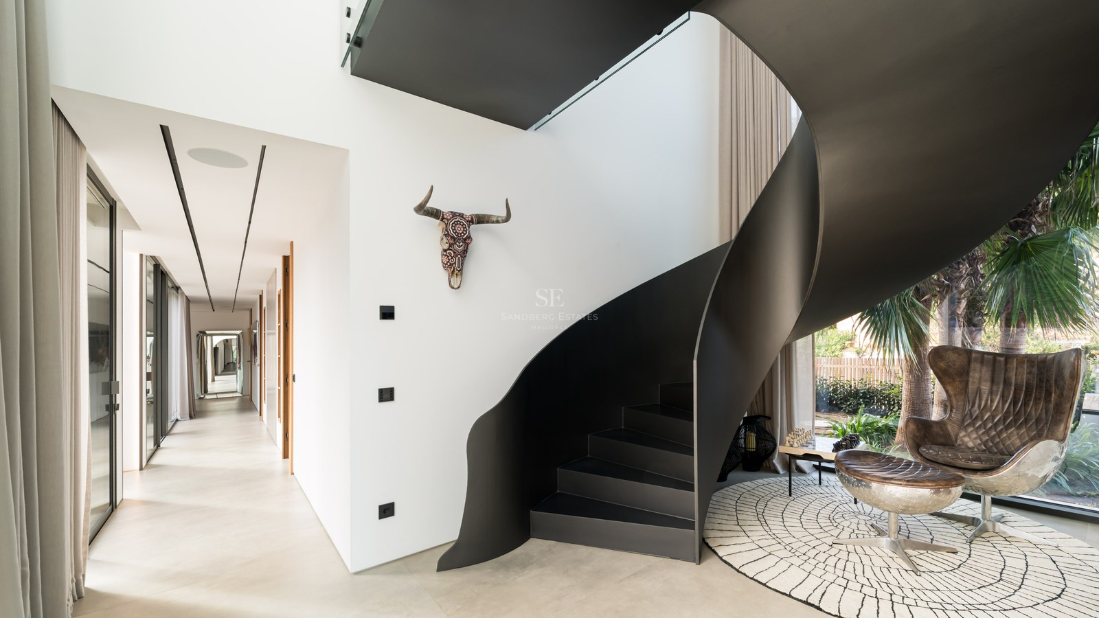Escalier en colimaçon moderne en métal noir mat dans une villa lumineuse aux murs blancs.