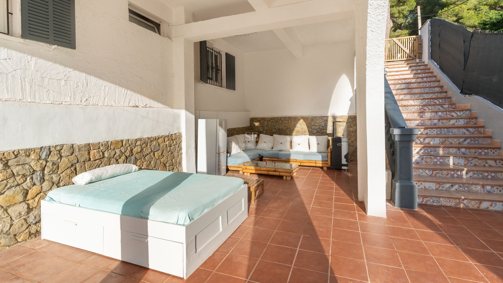 Covered terrace with terracotta floors, an outdoor daybed, lounge seating, stone walls, and stairs with patterned tiles.