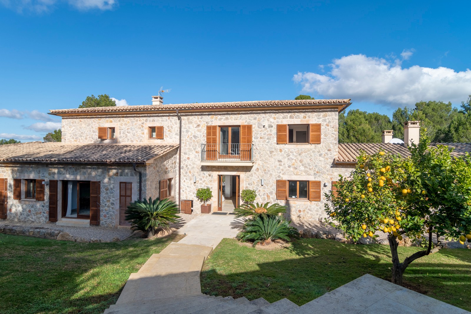 Villa de deux étages en pierre naturelle avec volets en bois marron, toit en terre cuite et un citronnier.