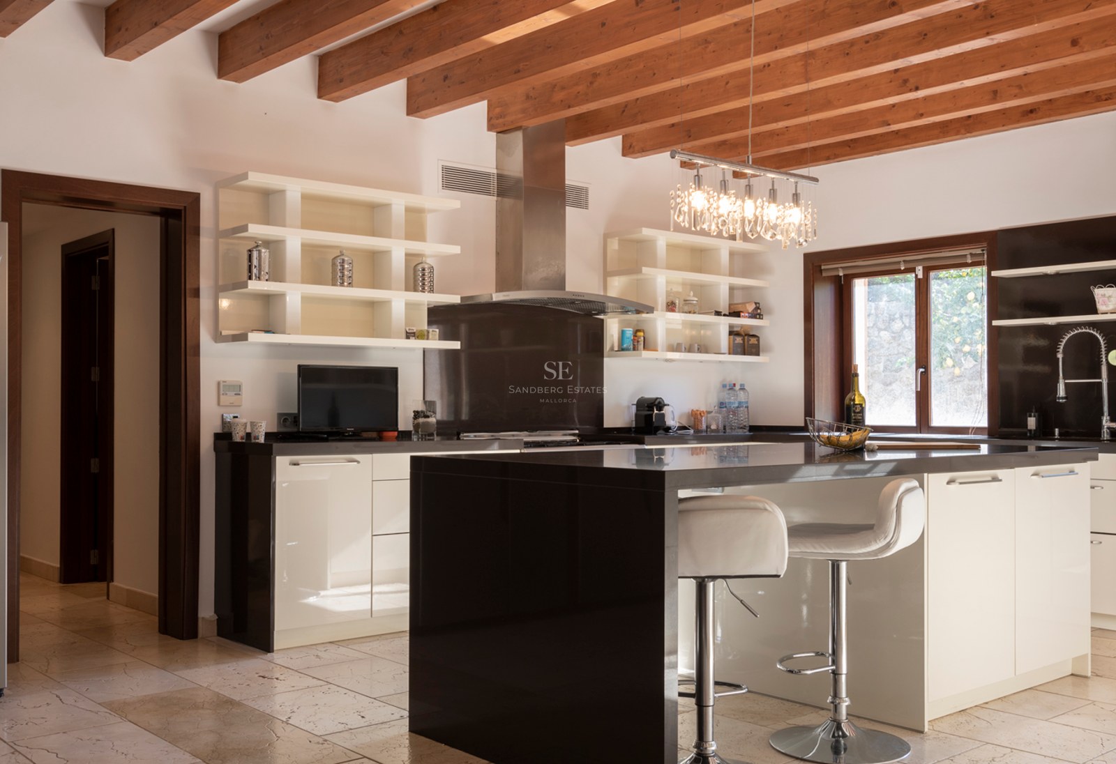 Cuisine moderne avec îlot noir, placards blancs, poutres en bois apparentes et sol en pierre naturelle.