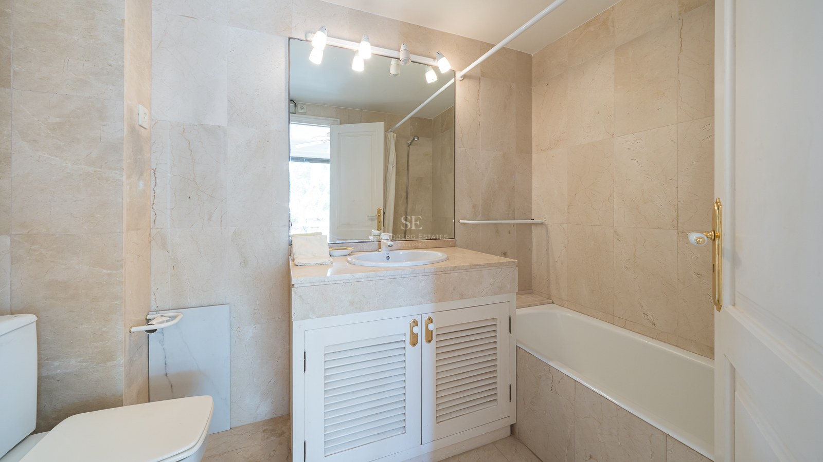 Salle de bains de style méditerranéen avec carrelage en marbre crème, baignoire intégrée et meuble vasque blanc.