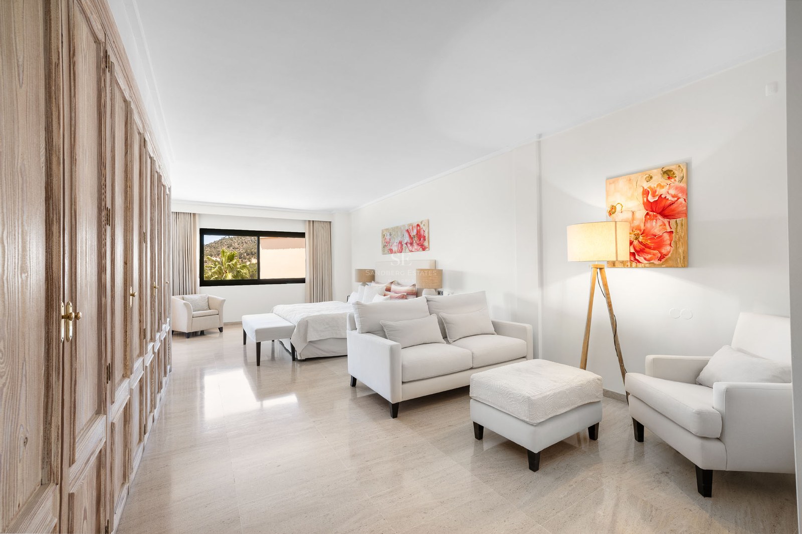 Suite lumineuse avec canapé blanc, armoires en bois, grand lit et art floral sur sol en marbre poli.