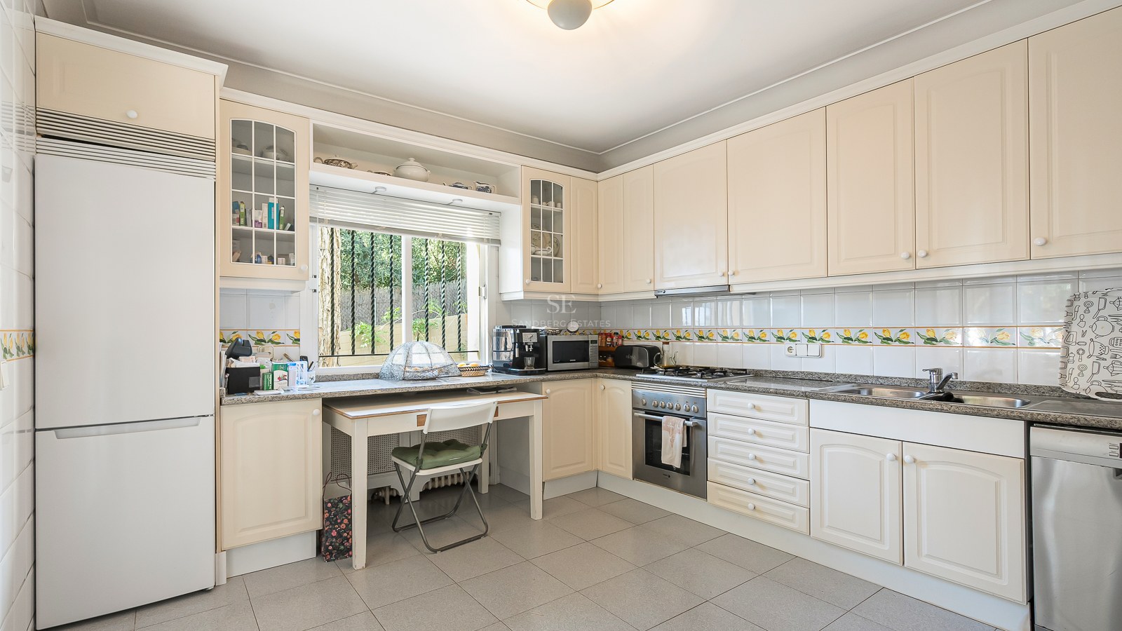 Amplia cocina crema con encimeras de granito, pequeña mesa junto a la ventana y electrodomésticos integrados.