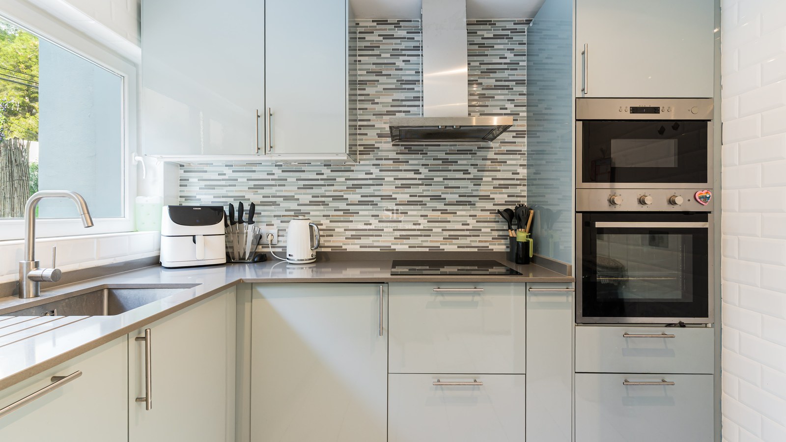 Modern kitchen featuring light blue cabinets, grey countertops, a mosaic tile backsplash, and stainless steel appliances.