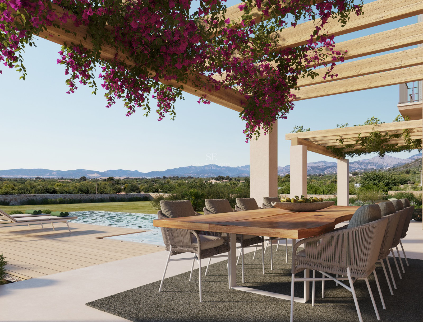 Table à manger en bois sous une pergola de bougainvilliers surplombant une piscine et des montagnes.
