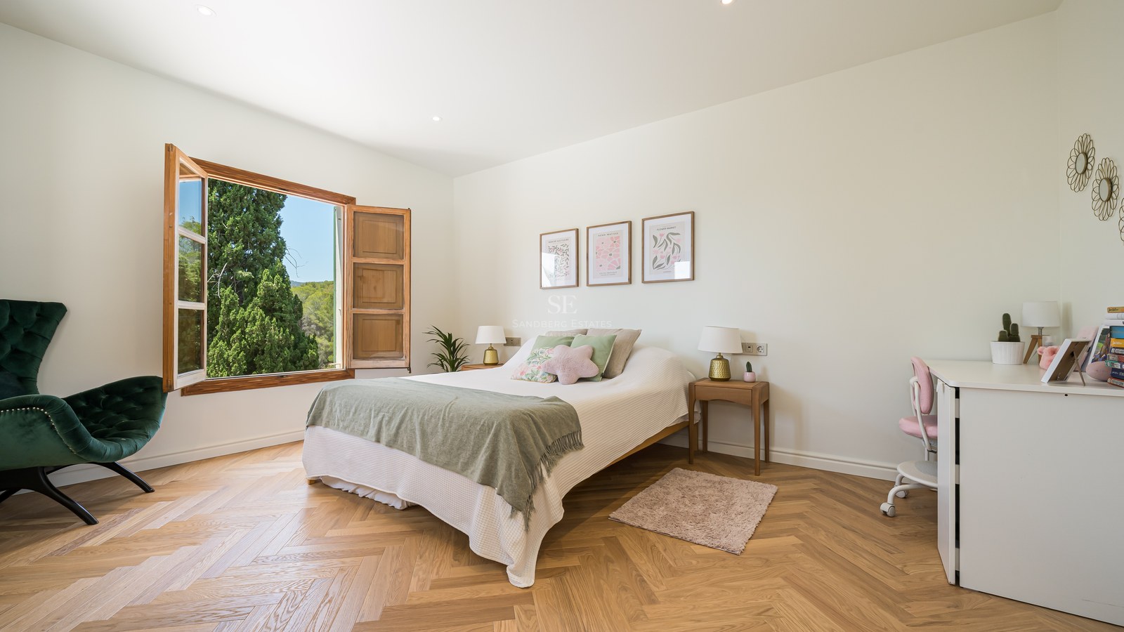 Bright bedroom featuring oak herringbone floors, a green velvet chair, and an open window looking onto lush trees.
