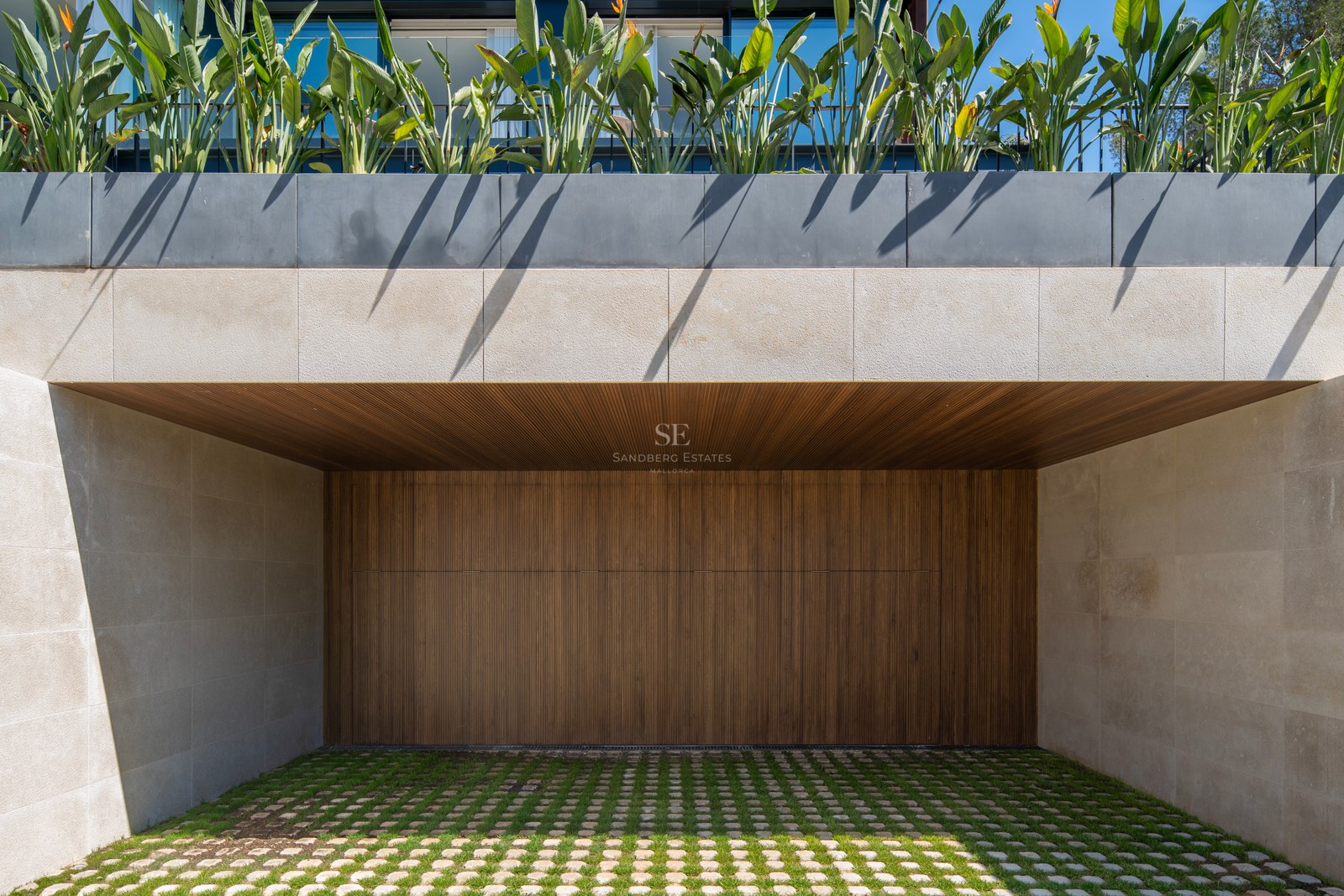 Entrée de garage contemporaine avec porte en bois à lattes, murs en pierre naturelle et pavés drainants végétalisés.