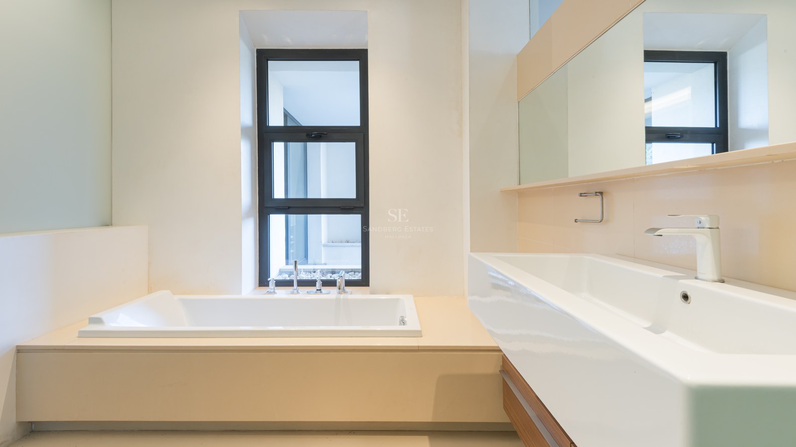 Modern bathroom featuring a built-in white bathtub next to a window and a large white rectangular sink with a wide mirror.