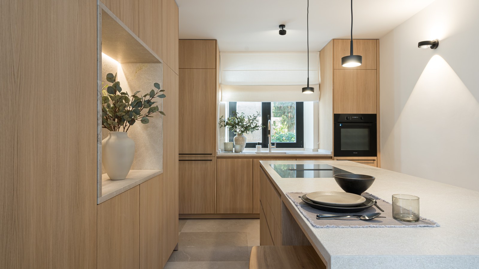 Cuisine moderne avec placards en chêne, îlot en pierre, suspensions minimalistes et niche décorative éclairée.
