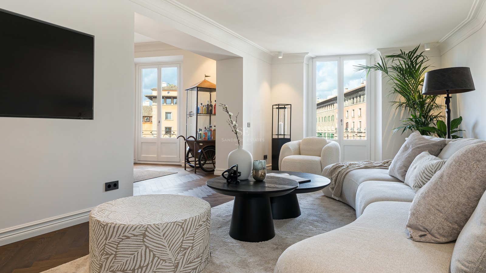Salón contemporáneo con sofá curvo blanco, mesas de centro negras y grandes ventanales con vistas urbanas.