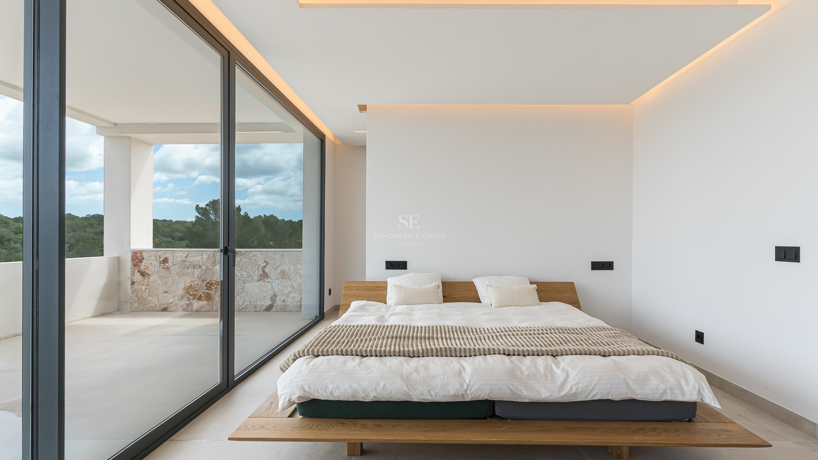 Minimalist master bedroom featuring a wooden bed frame, large glass sliding doors, and access to a stone-walled balcony.