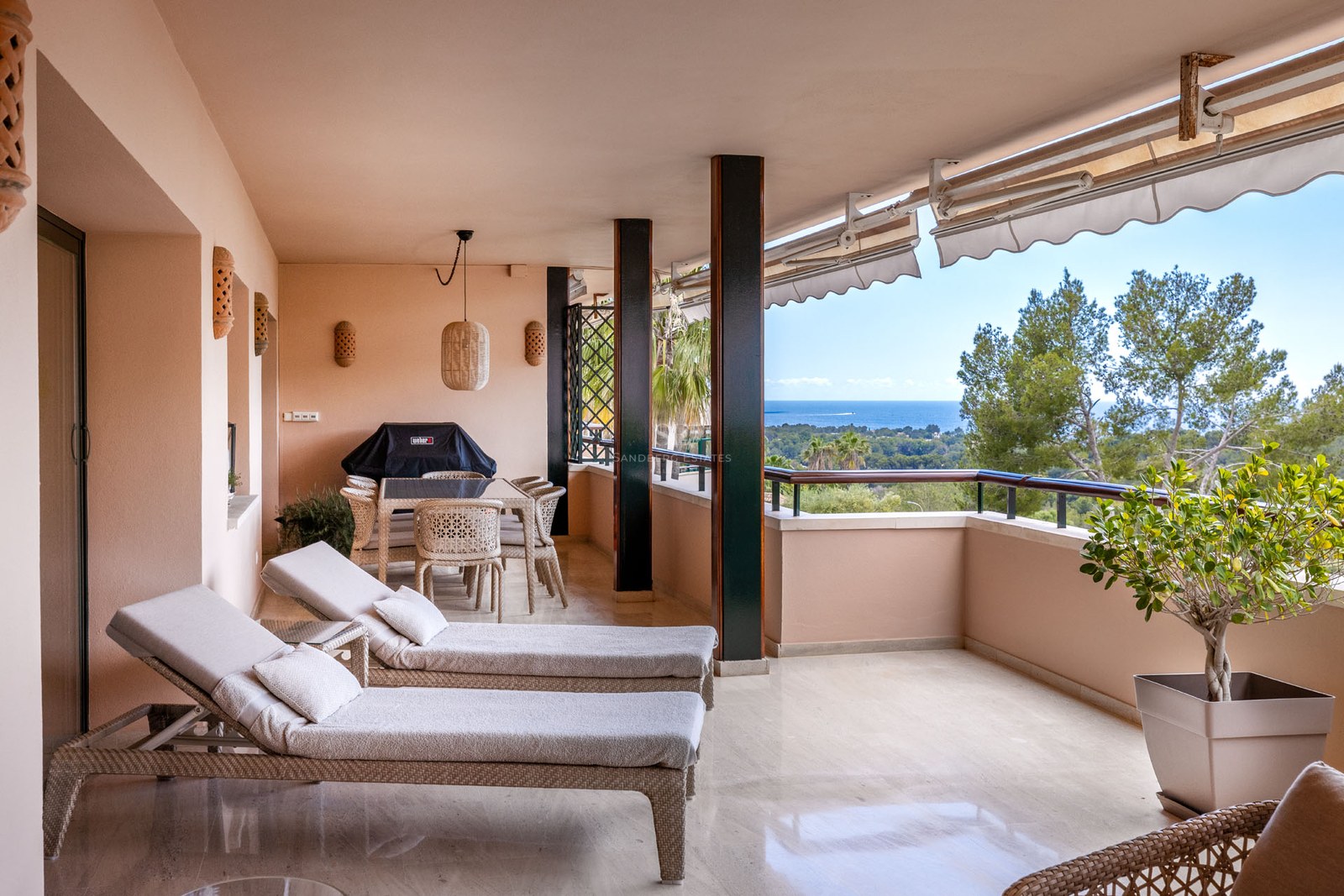 Terrasse couverte avec bains de soleil, salle à manger extérieure et vue sur la mer et la verdure.