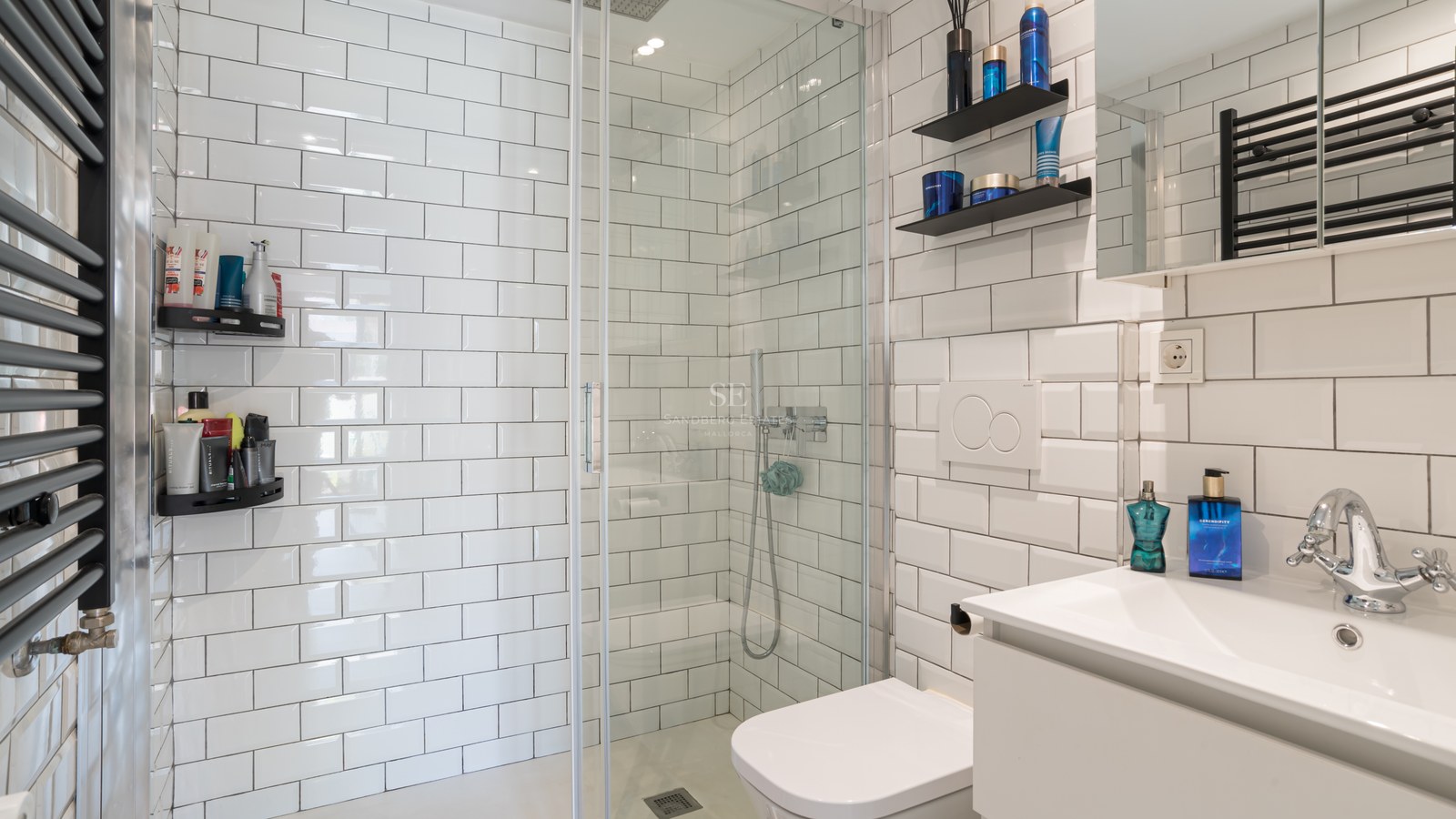 Baño moderno con azulejos blancos tipo metro, ducha de cristal, radiador negro y lavabo minimalista.