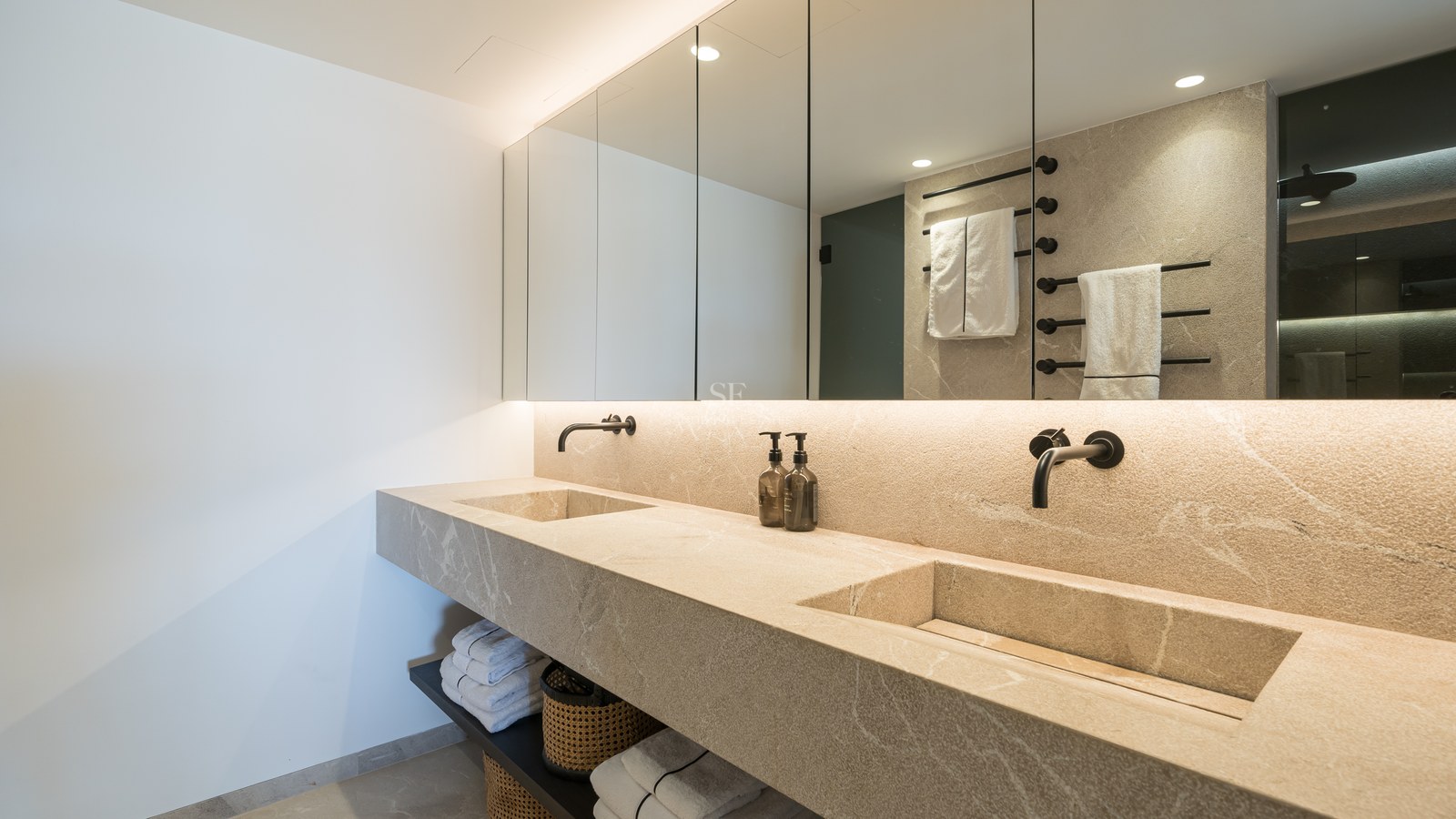 Salle de bain de luxe avec double vasque intégrée en pierre, miroirs rétroéclairés et robinetterie noire mate.