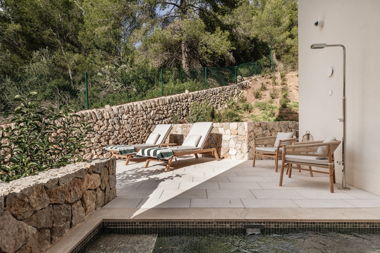 Terrasse moderne en pierre avec bains de soleil, douche extérieure en métal et vue sur une forêt dense.
