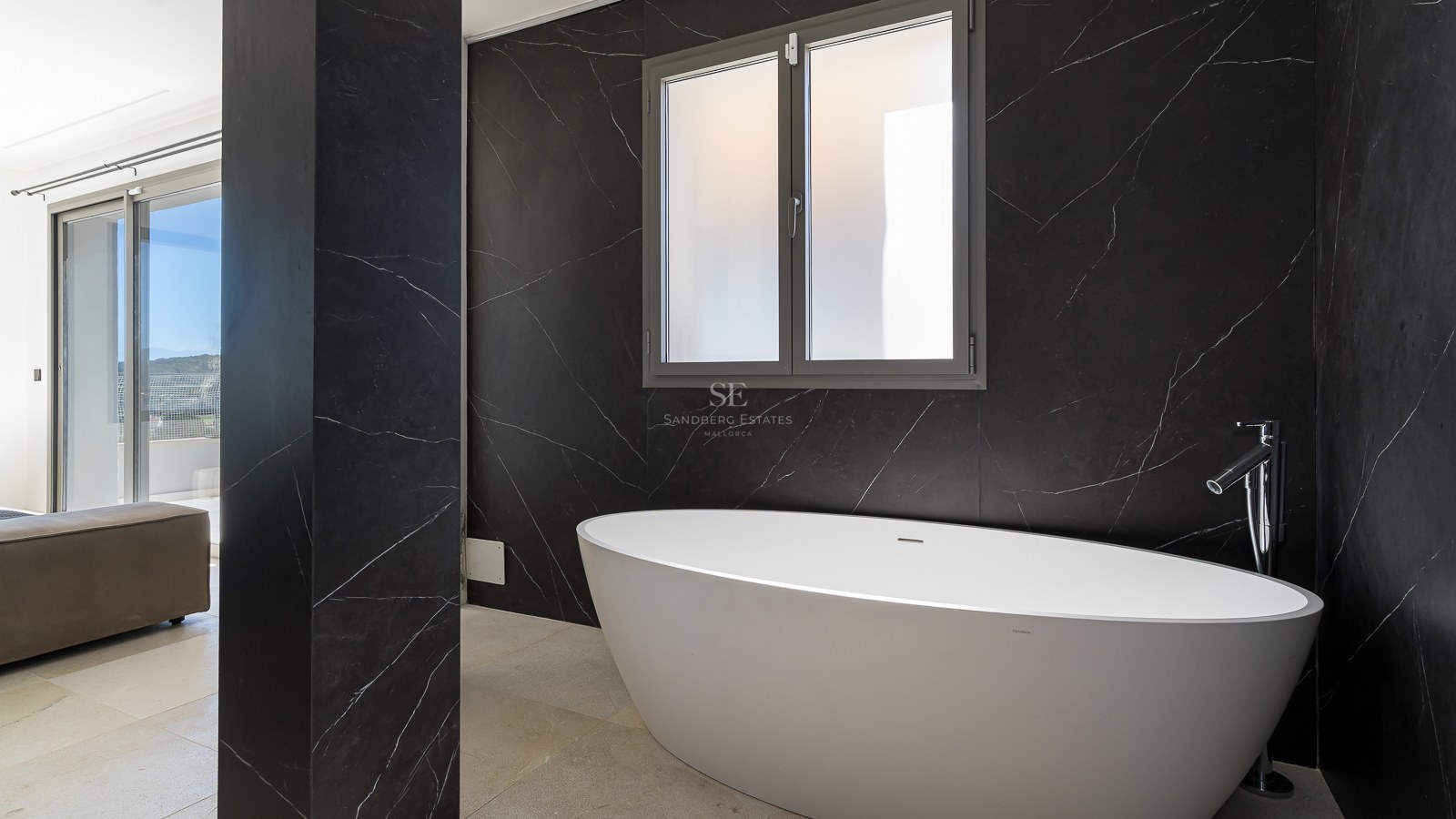 Modernes Badezimmer mit weißer ovaler Badewanne vor einer schwarzen Marmorwand mit weißen Adern.
