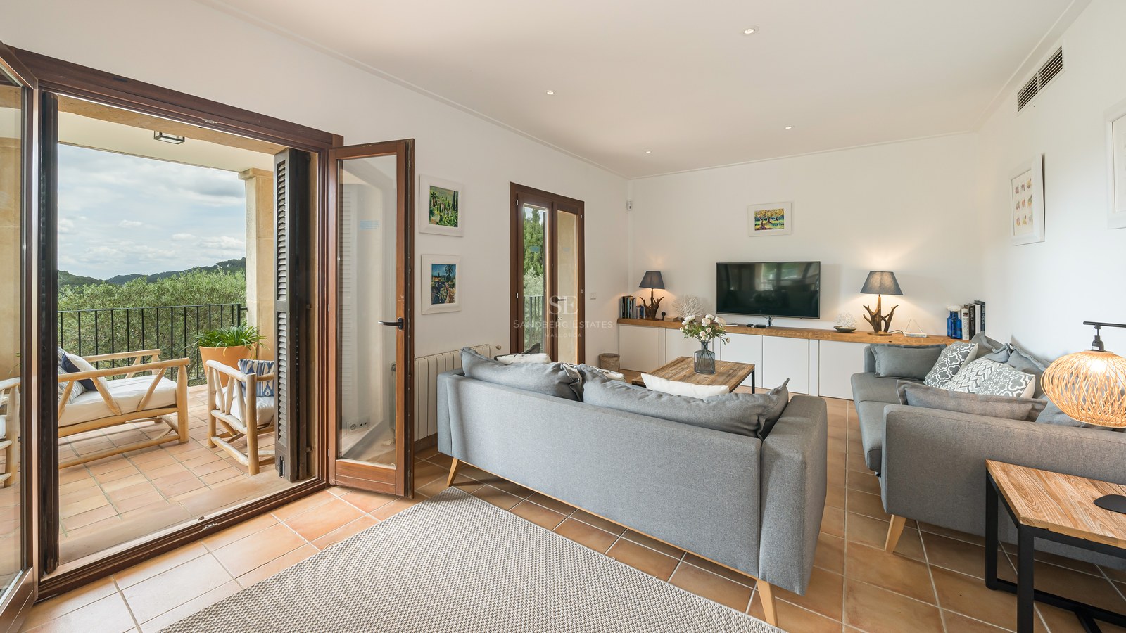 Modern grå soffa i ett vardagsrum med terrakottagolv och öppna trädörrar mot en terrass.