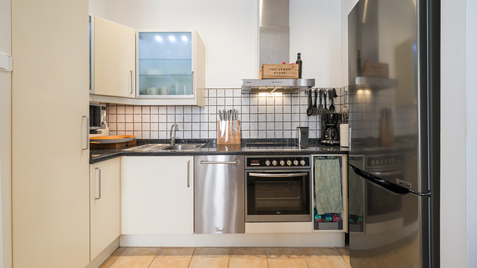 Cuisine moderne avec placards crème, électroménager en inox, plan de travail en granit noir et crédence en carrelage blanc.