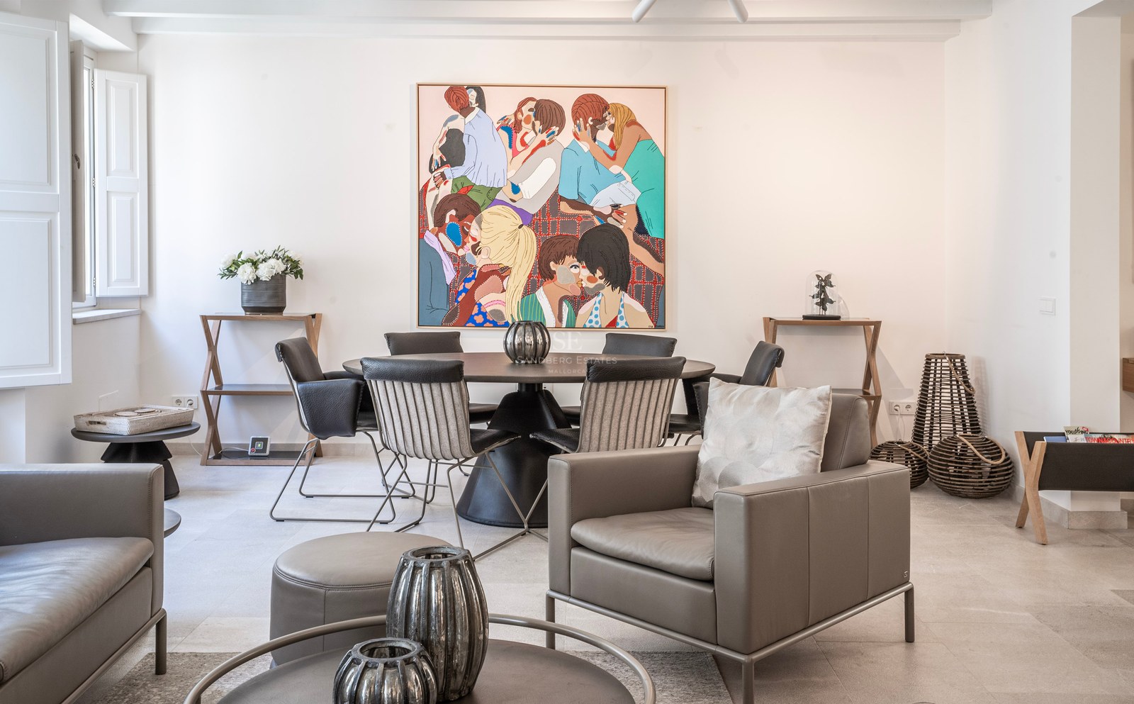 Bright modern room with a grey leather armchair, a round dining table, and a large colorful painting on the wall.