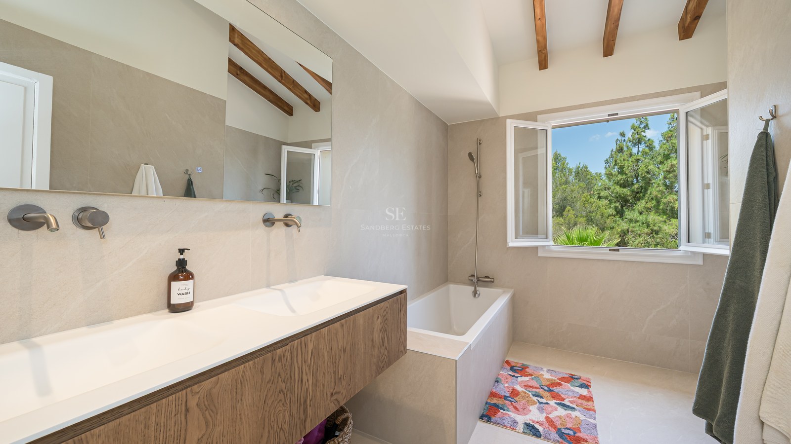 Contemporary bathroom featuring a wood vanity, double sink, and views of pine trees through an open window.