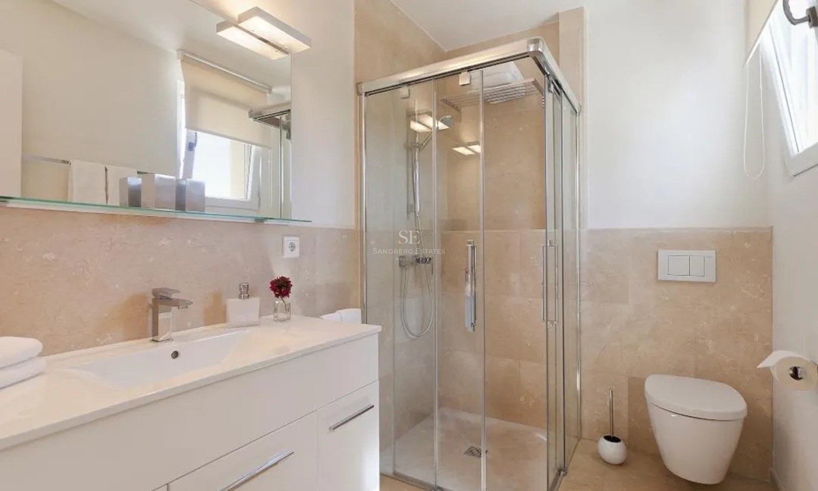 Modern bathroom featuring a glass shower, cream marble wall tiles, white vanity, and wall-hung toilet.
