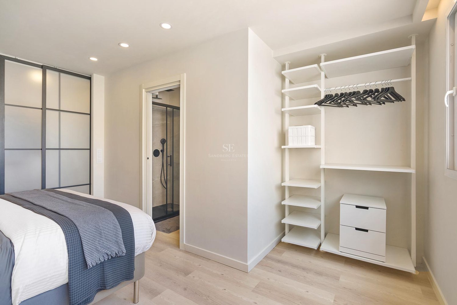 Chambre contemporaine lumineuse avec système de dressing blanc, parquet clair et aperçu de la salle de bain attenante.