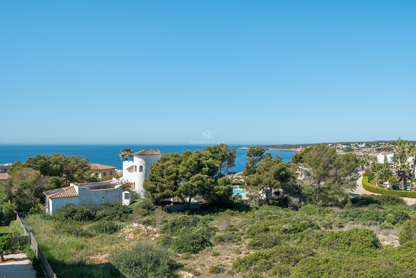 Vue en plongée de la mer Méditerranée bleue derrière des arbres verts et des villas méditerranéennes blanches.