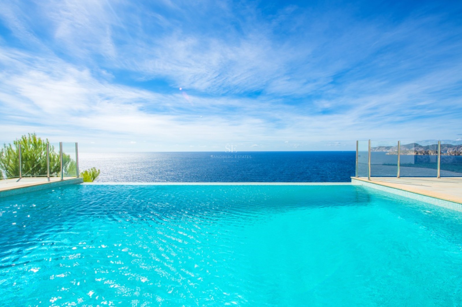 Lyxig infinitypool med utsikt över Medelhavet, glasräcken och klarblå himmel.
