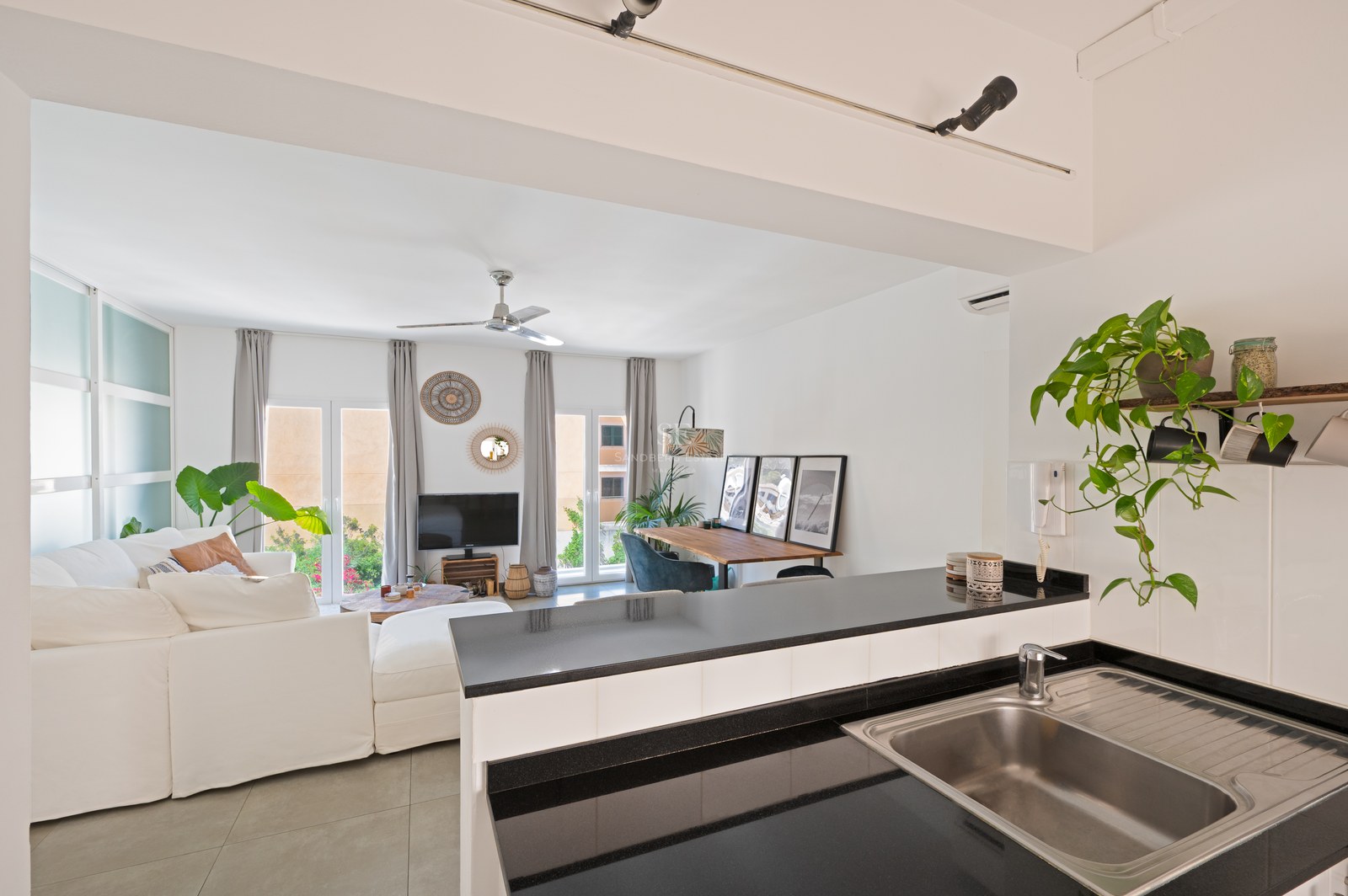 View from a kitchen counter into a bright living room with a large white sofa, dining area, and glass patio doors.