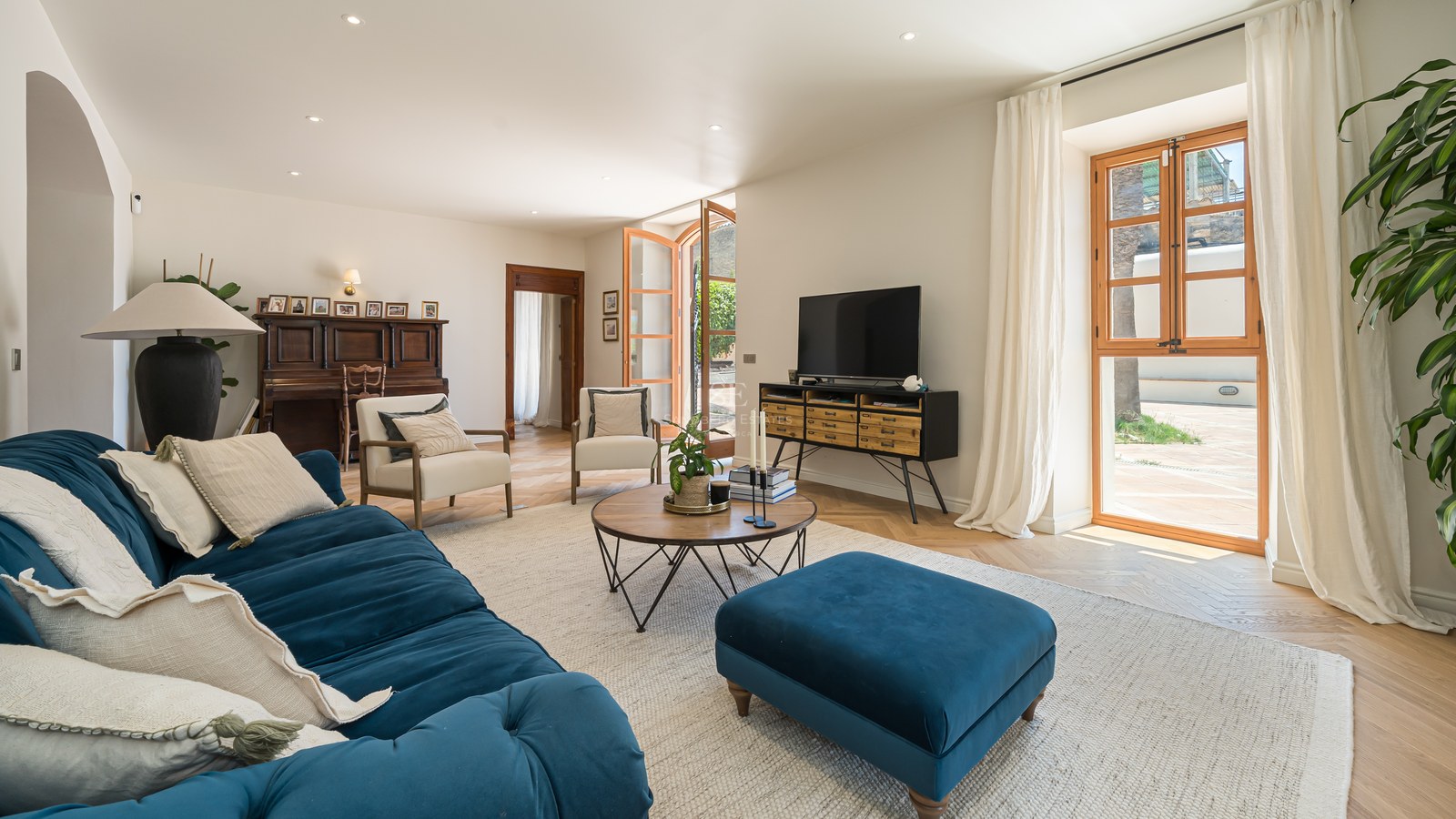 Spacious living room featuring a teal velvet sofa, oak herringbone floors, and large wooden-framed windows to a terrace.