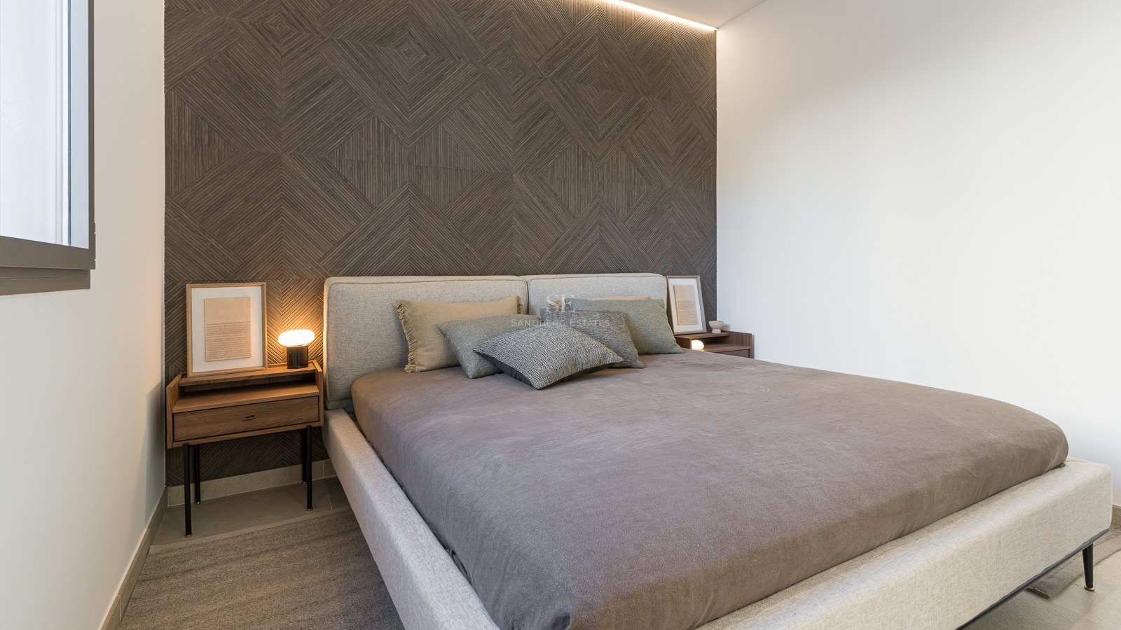 Zeitgenössisches Schlafzimmer mit geometrischer Holzakzentwand, gepolstertem Bett und Nachttischen aus Walnussholz.