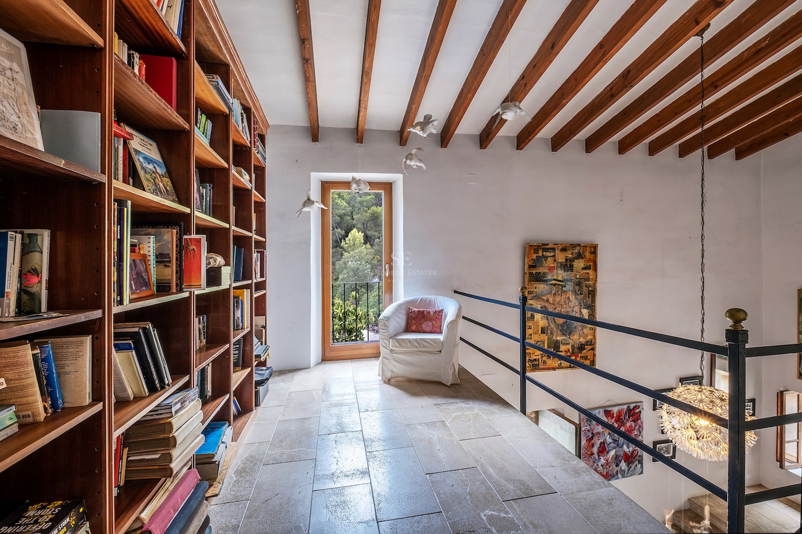Bibliothèque en mezzanine avec étagères en bois du sol au plafond, sol en pierre et poutres apparentes.
